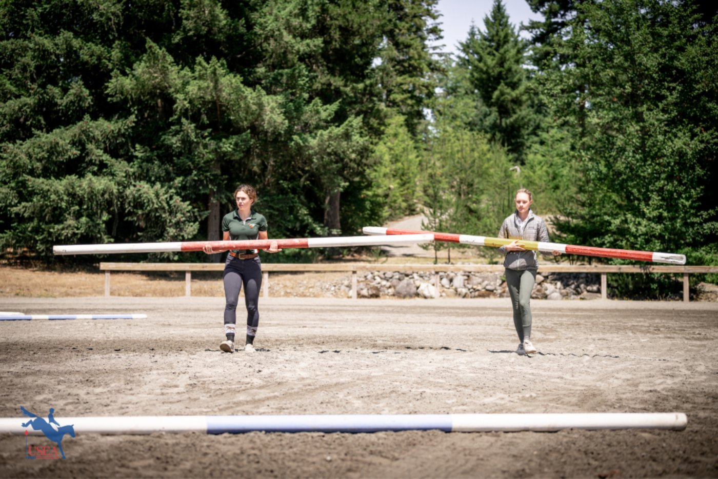 Alexa Marandas and Natalie Barlow carry poles to set the show jumping course. USEA/Cortney Drake photo